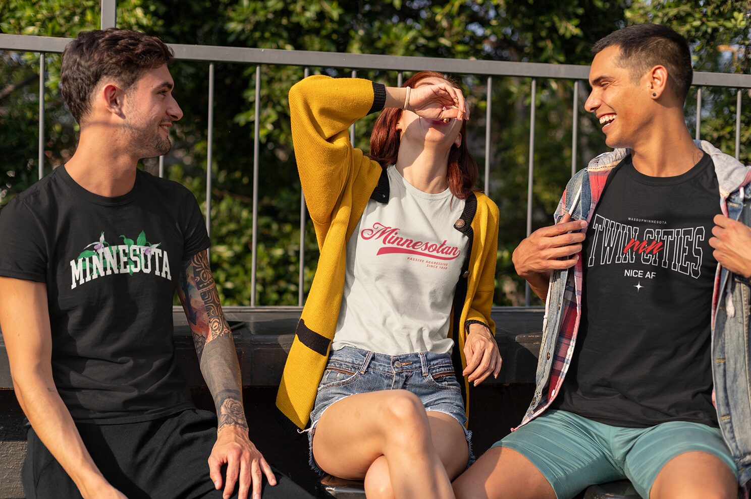 Three friends laughing on a sunny patio wearing Wassup Minnesota tees